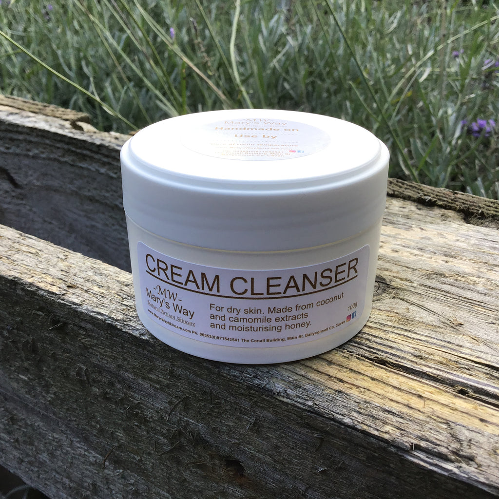 Jar of cream cleanser resting on wooden pallet with foilage in background.