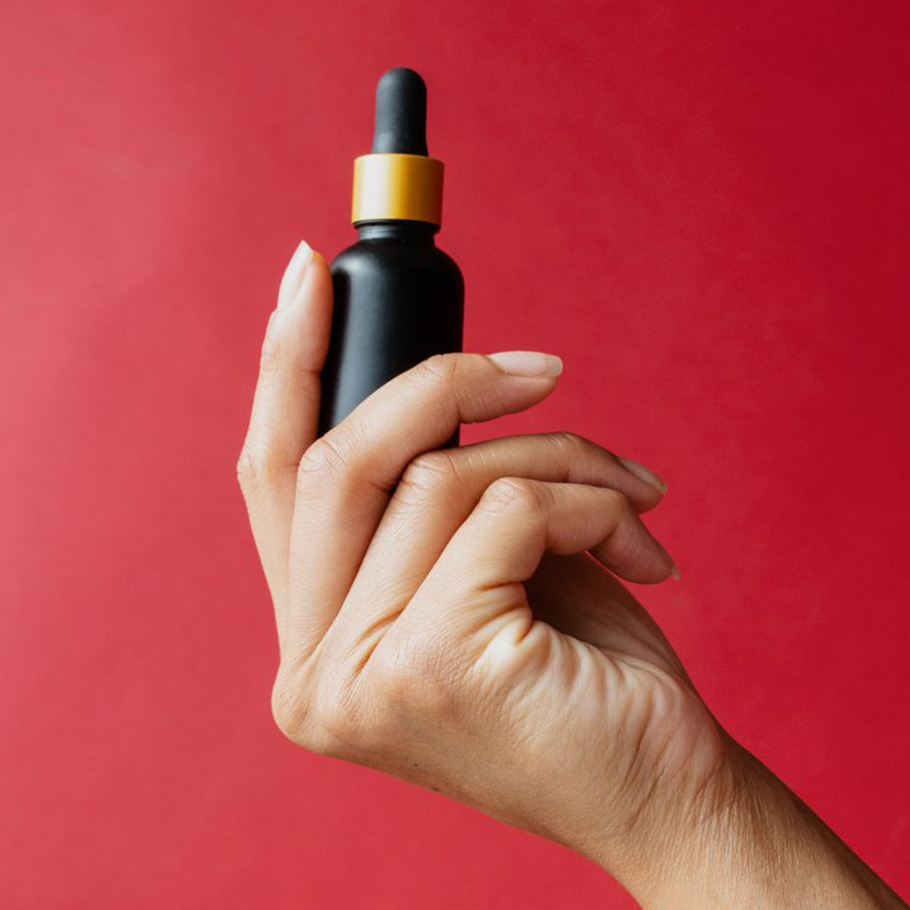 Hand holding droplet brown bottle with red background.
