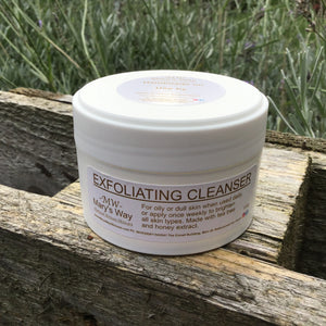Jar of marys way exfoliating  cleanser resting on wooden pallet with foilage in background.
