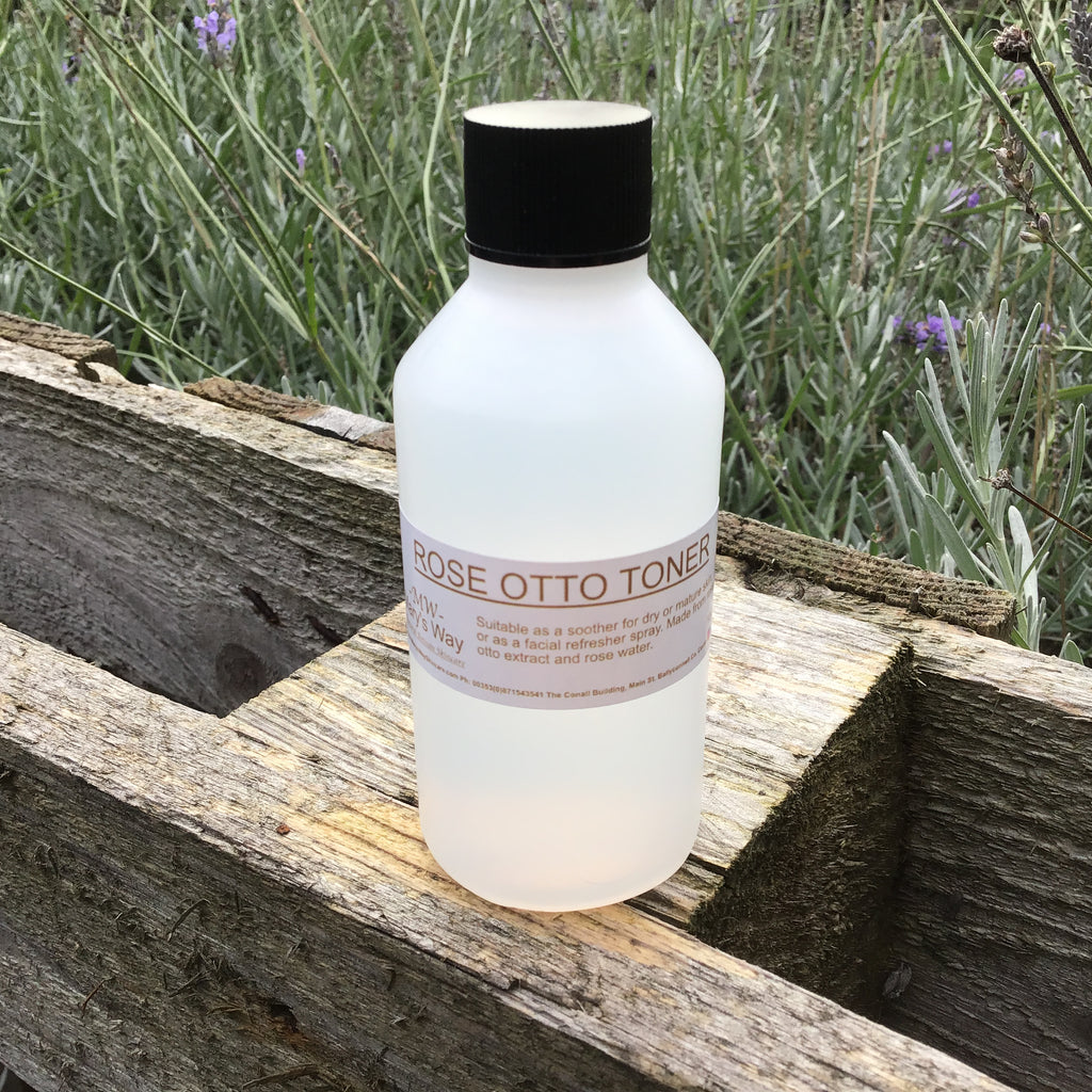 Bottle of Mary's Way rose Otto toner resting on wooden pallet with foilage in background.