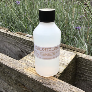 Bottle of Mary's Way rose Otto toner resting on wooden pallet with foilage in background.